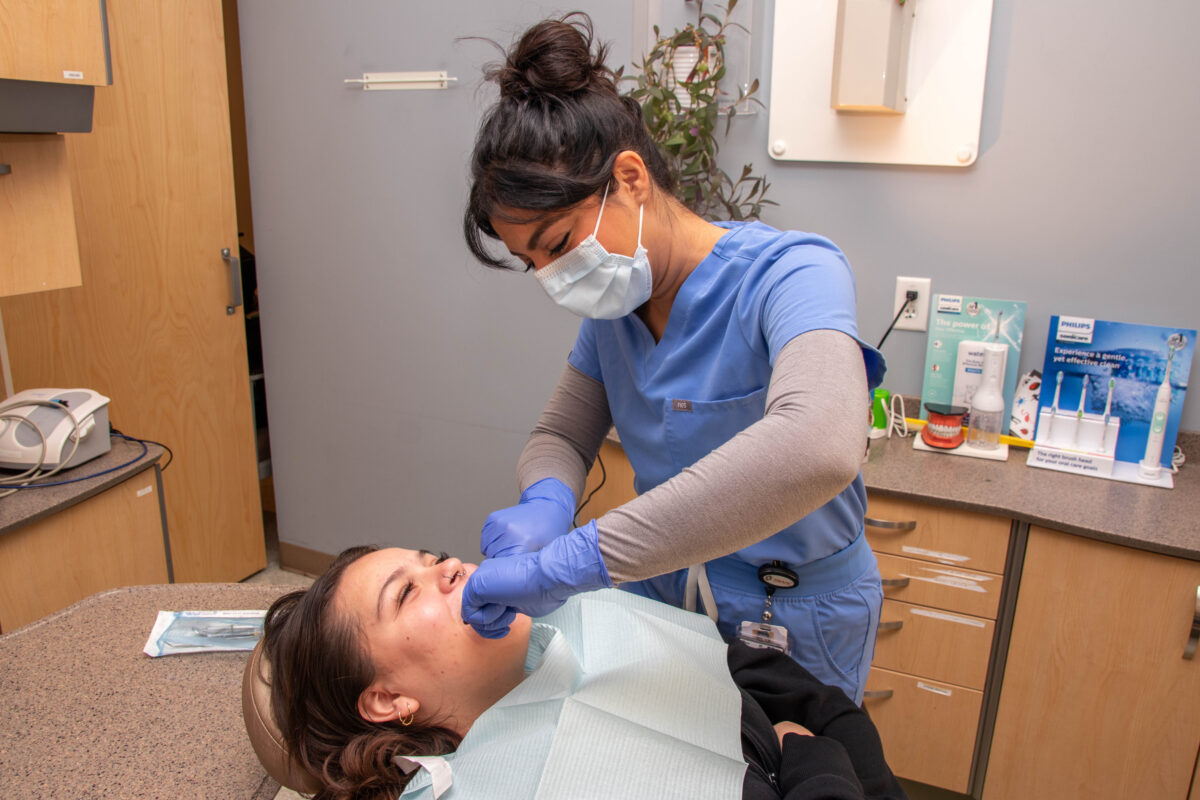 A dental hygienist working inside of a patient's mouth as they lay in the chair in front of the dental hygienist 